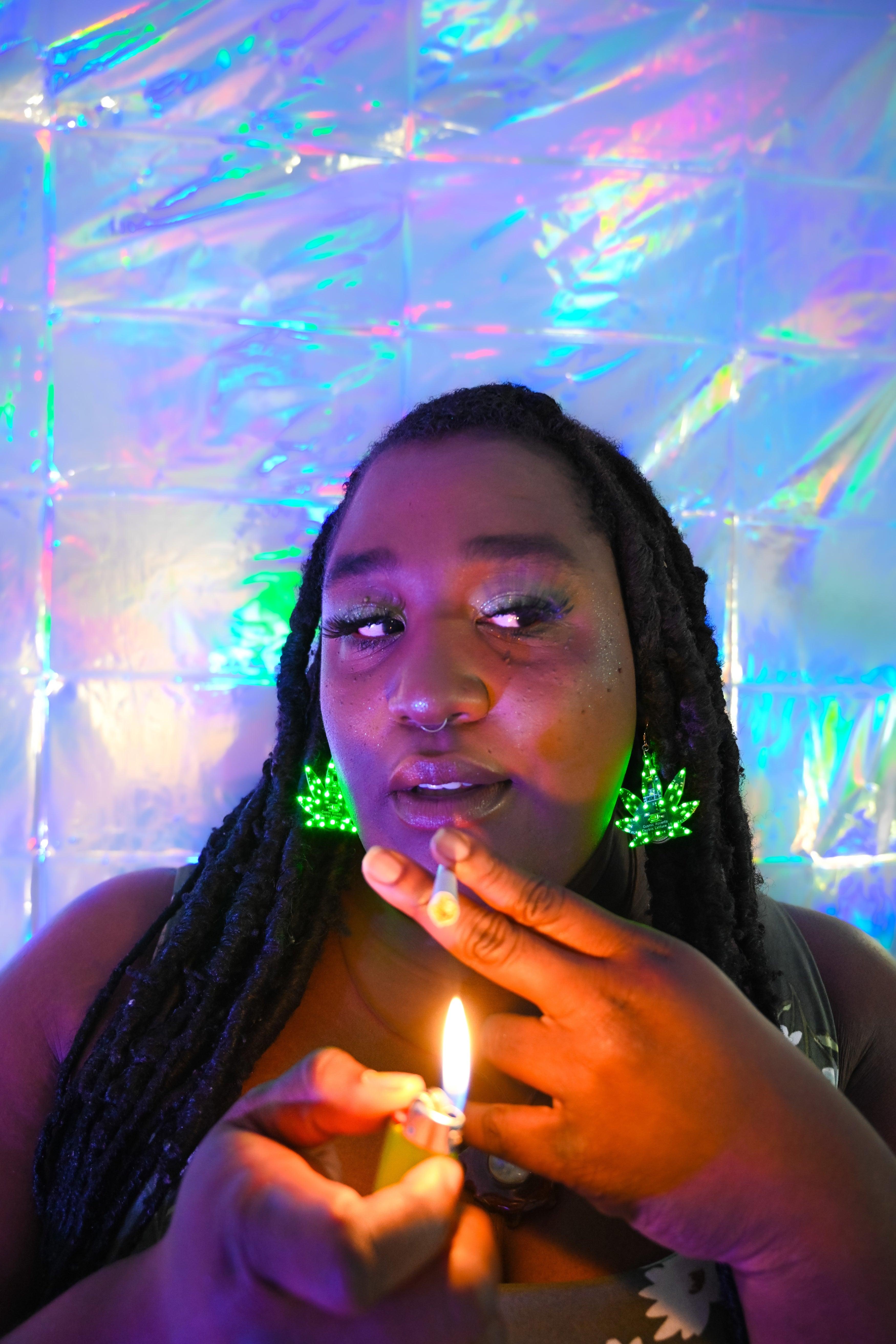 A young woman lights a joint while wearing marijuana-shaped LED earrings.