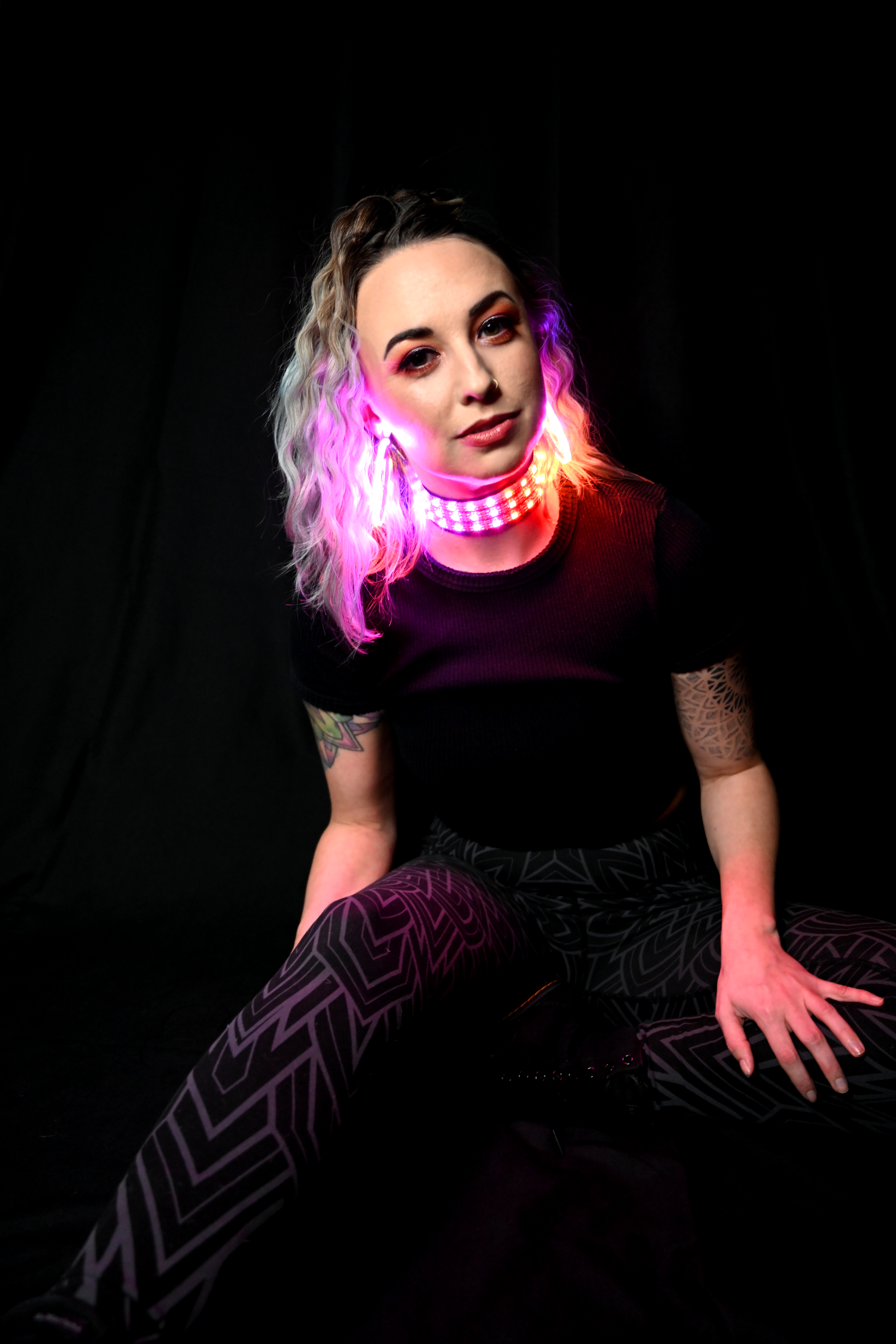 model in a sitting pose wearing led choker and led earrings w/ black background